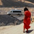 A woman looks down at her feet and her van is parked in the distance in the desert.