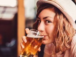 Close up of a woman with natural curly hair drinking a pint of beer.