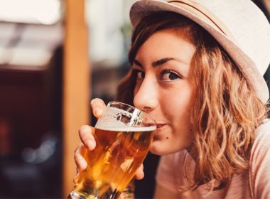 Close up of a woman with natural curly hair drinking a pint of beer.
