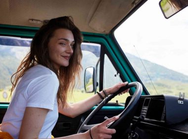 A young woman drives a camper van on a sunny day in nature.