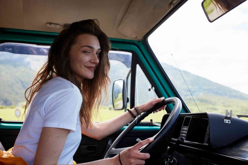 A young woman drives a camper van on a sunny day in nature.