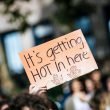 A hand holds up a sign reading "It's getting hot in here" at a climate change rally.