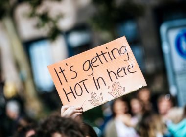 A hand holds up a sign reading "It's getting hot in here" at a climate change rally.