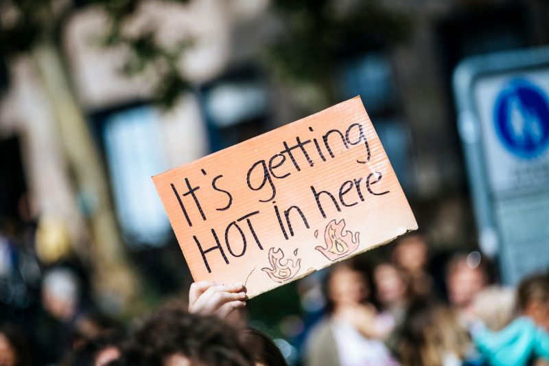 A hand holds up a sign reading "It's getting hot in here" at a climate change rally.