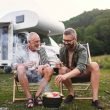 An adult man and his father share a beer while they cook food over the father at an RV Park.