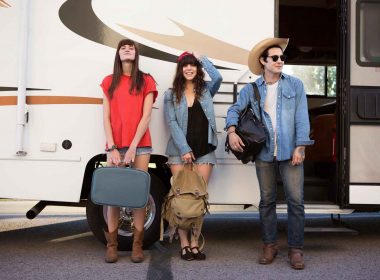 Three friends standing with their luggage in front of an RV, ready to go on a cross country trip.