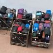 Several large metal crates filled with luggage outside of an airport.