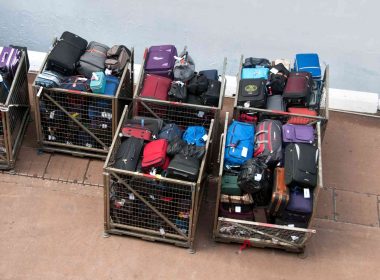 Several large metal crates filled with luggage outside of an airport.