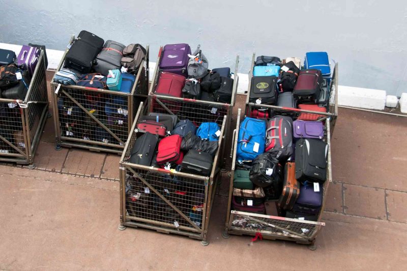 Several large metal crates filled with luggage outside of an airport.