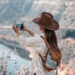A woman captures a breathtaking view of a lake from high up in the mountains using her mobile phone.