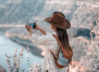 A woman captures a breathtaking view of a lake from high up in the mountains using her mobile phone.