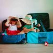 Two little girls sitting in suitcases playing with the packed hats and binoculars.