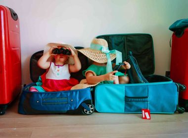 Two little girls sitting in suitcases playing with the packed hats and binoculars.