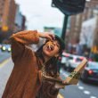 A woman eating toppings and cheese from a New York style pizza as she walks along a city street.