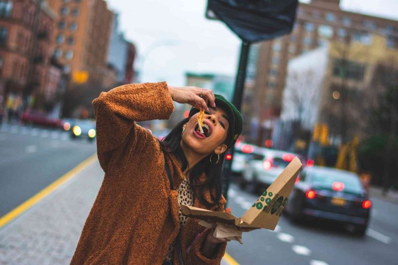 A woman eating toppings and cheese from a New York style pizza as she walks along a city street.