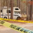Yellow tape marking off a crime scene around an RV in a wooded campground.