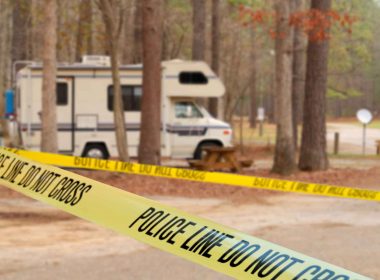 Yellow tape marking off a crime scene around an RV in a wooded campground.