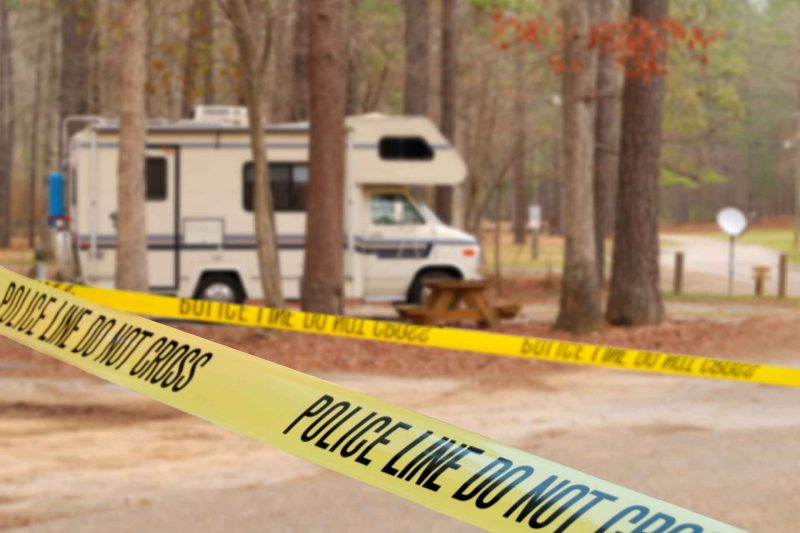 Yellow tape marking off a crime scene around an RV in a wooded campground.