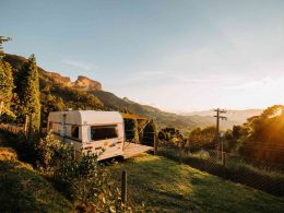 A stationary travel trailer parked ona hillside with a terrace attached overlooking the sunset.