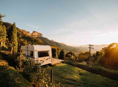 A stationary travel trailer parked ona hillside with a terrace attached overlooking the sunset.