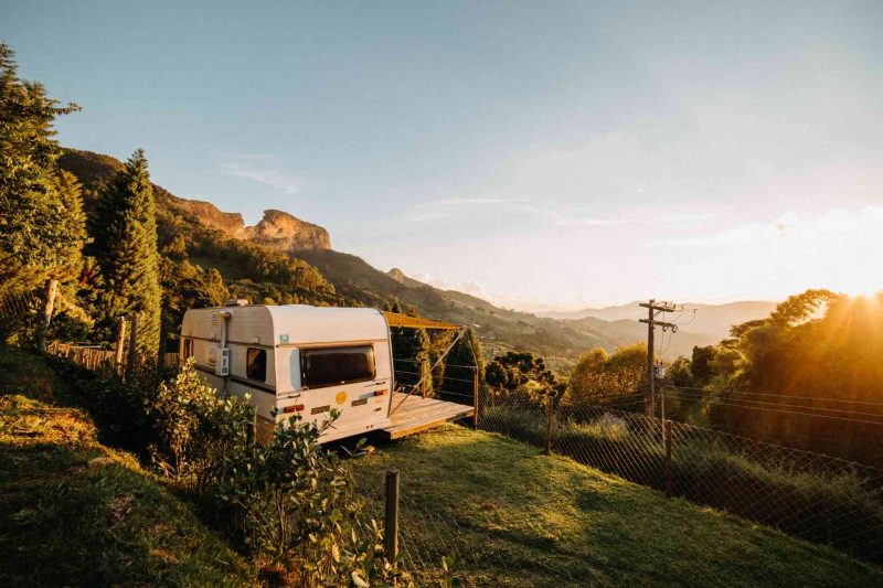 A stationary travel trailer parked ona hillside with a terrace attached overlooking the sunset.