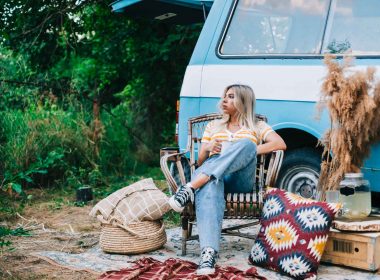 A woman sits outside of her vintage camper van looking unhappy.