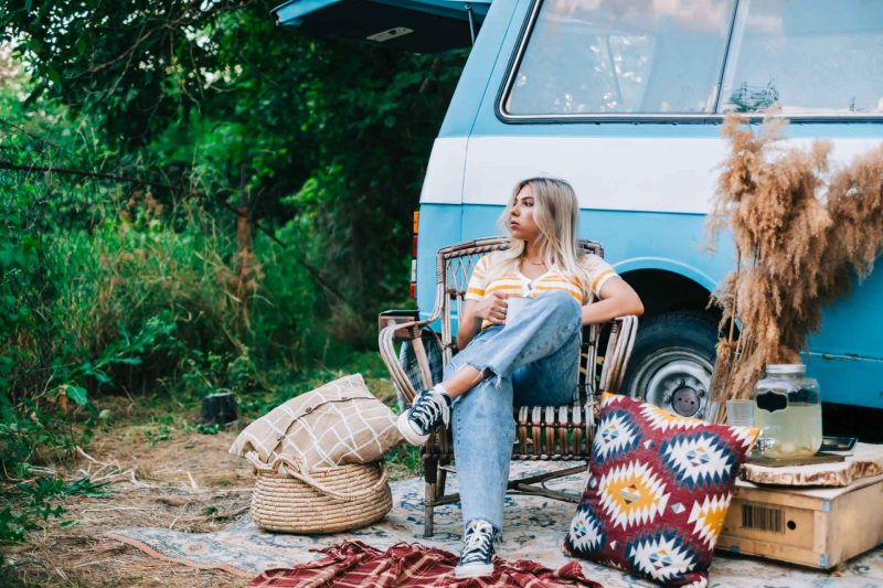 A woman sits outside of her vintage camper van looking unhappy.