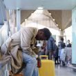 A stresses traveler puts his head in his hand and slouches while sitting in an airport.