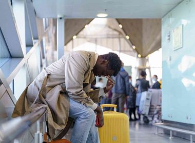 A stresses traveler puts his head in his hand and slouches while sitting in an airport.