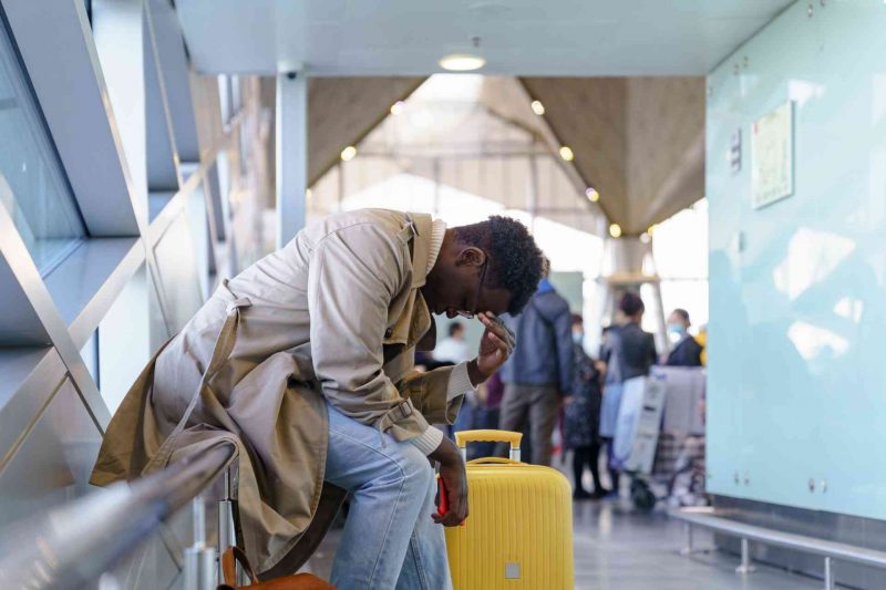A stresses traveler puts his head in his hand and slouches while sitting in an airport.