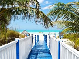 Walking down a blue and white board walk to a white sandy beach in the tropics.