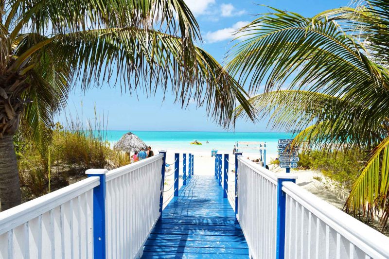 Walking down a blue and white board walk to a white sandy beach in the tropics.
