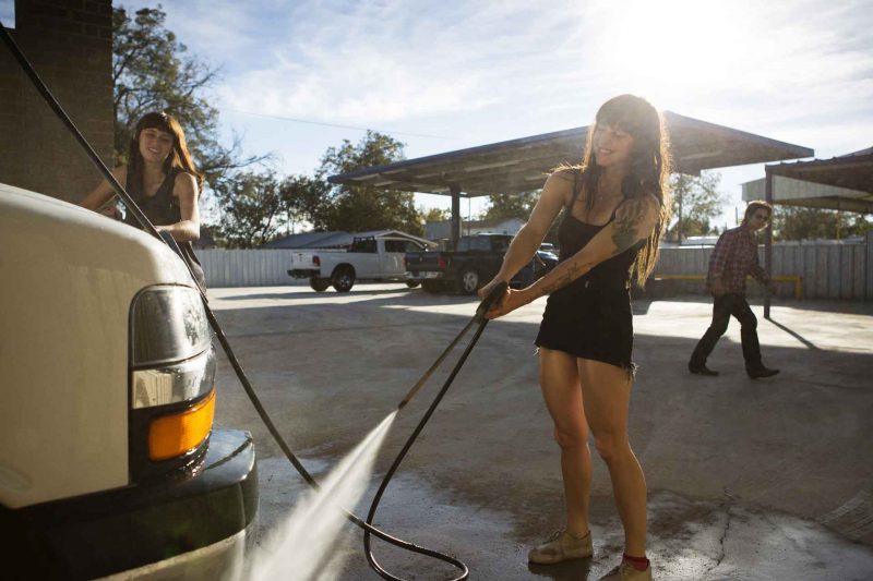 A young woman power washes her camper van.