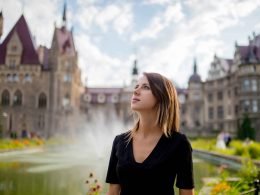 A woman in a garden in front of a grand castle.