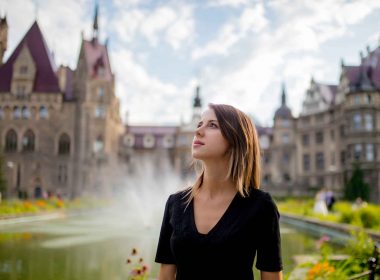A woman in a garden in front of a grand castle.