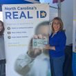 Two women stand in from of a REAL ID banner and one holds up her new Star ID.