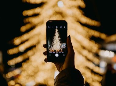 A mobile phone photographing Christmas tree lights at night in the city.