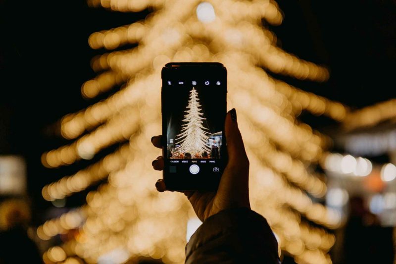 A mobile phone photographing Christmas tree lights at night in the city.