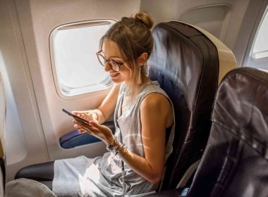 A happy woman traveler sitting in her plan seat with sun coming through the window.