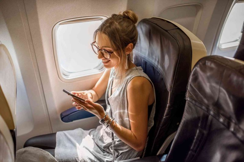A happy woman traveler sitting in her plan seat with sun coming through the window.
