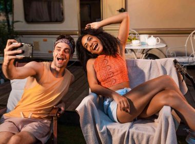 Two overly happy RVers self recording a video in front of their travel trailer.