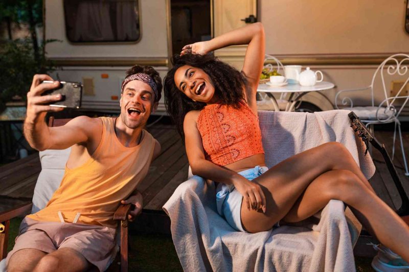Two overly happy RVers self recording a video in front of their travel trailer.