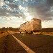A motorhome RV drives down the highway and the sun fades in and out of clouds.