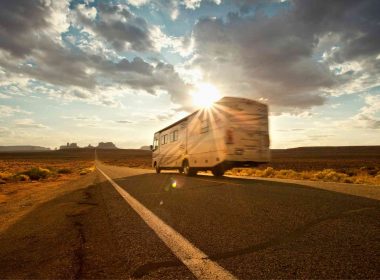 A motorhome RV drives down the highway and the sun fades in and out of clouds.