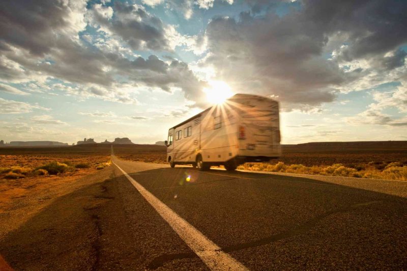 A motorhome RV drives down the highway and the sun fades in and out of clouds.
