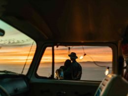 A couple embraces each other for comfort as they watch the sun set standing outside of the their camper.