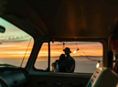 A couple embraces each other for comfort as they watch the sun set standing outside of the their camper.