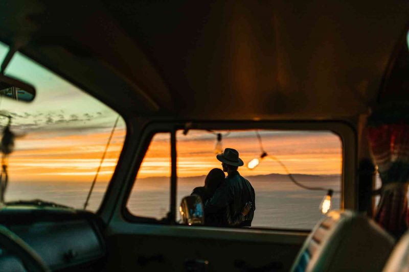 A couple embraces each other for comfort as they watch the sun set standing outside of the their camper.