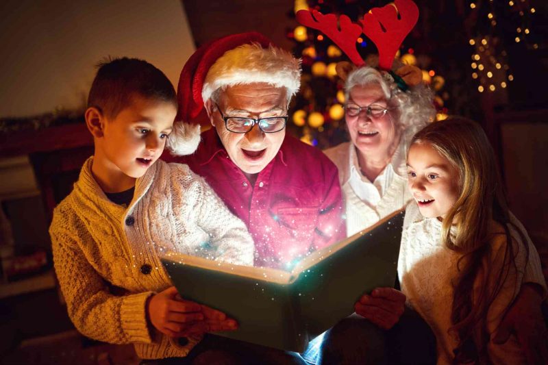 Grandparents and grandkids enjoying the magic of Christmas as they read a book together.