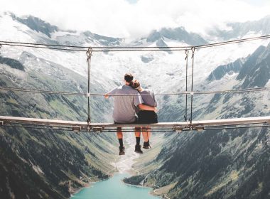 A couple rests on a suspension bridge over a ravine in the mountains enjoying a spectacular view.